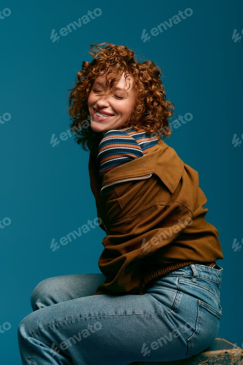 Preview: Stylish young woman with curly hair smiles effortlessly against a vibrant blue backdrop