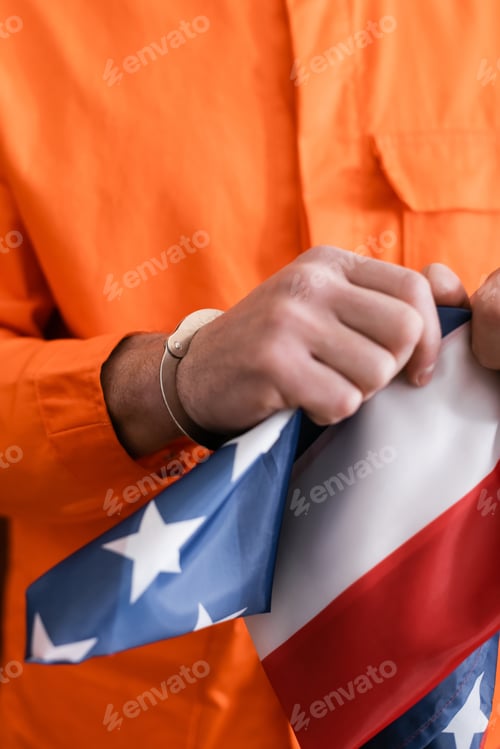 Preview: Cropped View of Man in Jail Uniform and Handcuffs Tearing American Flag, Justice Concept