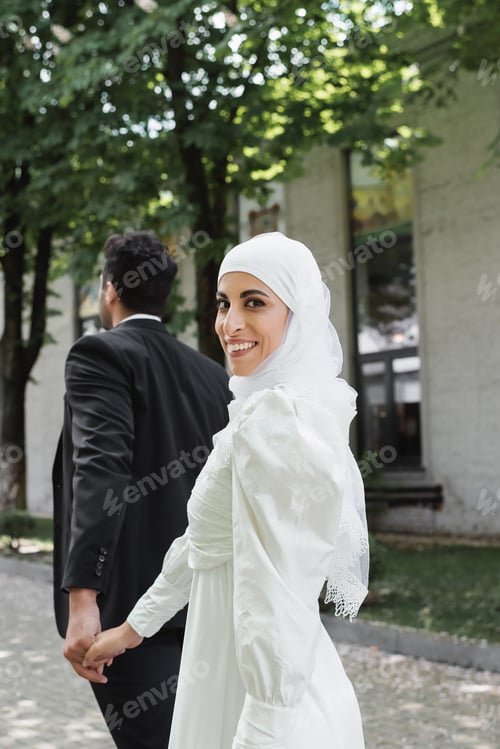 Preview: Joyful Muslim Bride in Wedding Dress Holding Hands With Groom in Suit