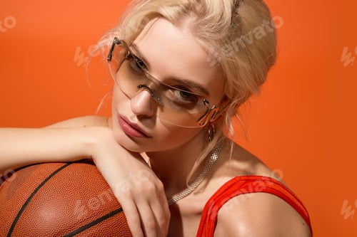 Preview: Beautiful young woman enjoying summer vibes with a basketball against vibrant orange backdrop