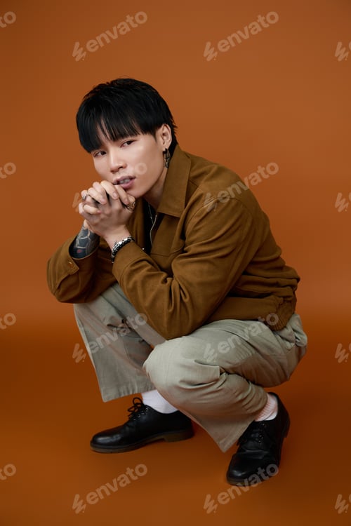 Preview: Young handsome man posing gracefully in a stylish outfit against a warm background