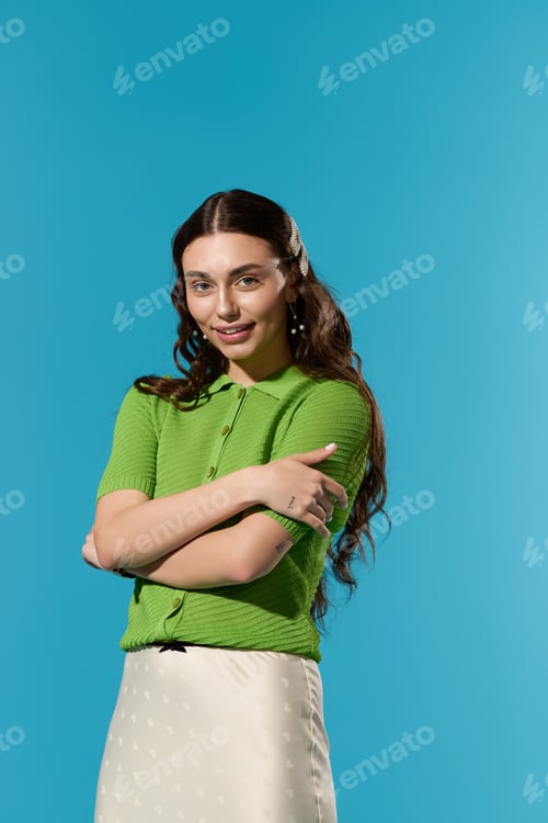 Preview: Stylish young woman poses confidently against a vibrant blue backdrop in chic green attire