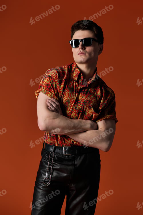 Preview: Confident young man showcasing bold fashion against a striking orange backdrop