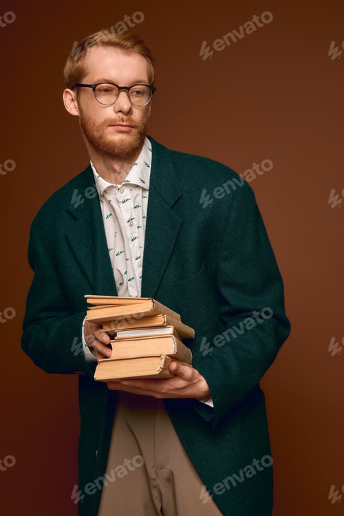 Preview: Charming red haired man showcasing unique style while holding classic books
