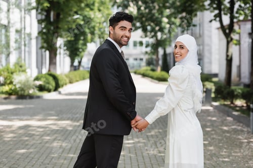 Preview: Happy Groom Holding Hands With Smiling Muslim Bride in Wedding Dress and Walking Together