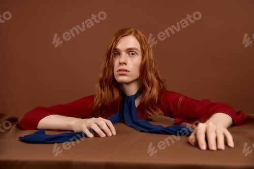 Preview: Handsome young man exudes elegance in stylish red attire with flowing red hair and blue accents