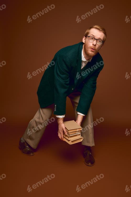 Preview: Stylish red haired man balances books in a stunning, artistic pose