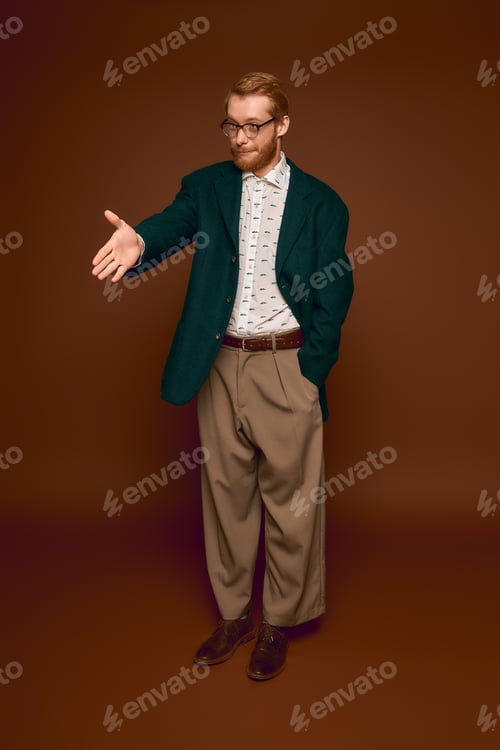 Preview: Stylish red haired man in elegant attire offers a warm handshake in a rich brown setting
