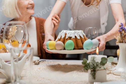 Preview: Partial View of Woman Holding Easter Cake and Painted Eggs Near Senior Mother During Festive Dinner