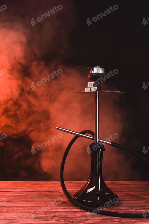Preview: Hookah with coals on wooden surface on black background with red smoke