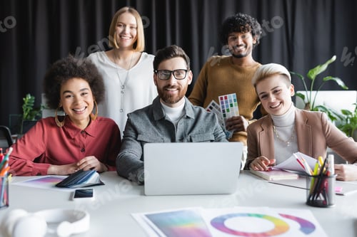 Preview: Happy Multiethnic Advertising Designers Looking at Camera Near Laptop and Color Samples