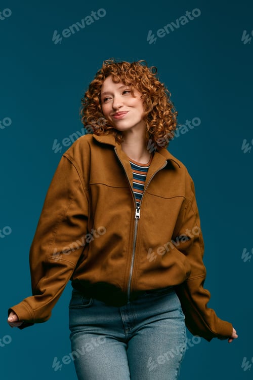 Preview: Stylish young woman poses confidently with a playful smile against a vibrant blue backdrop