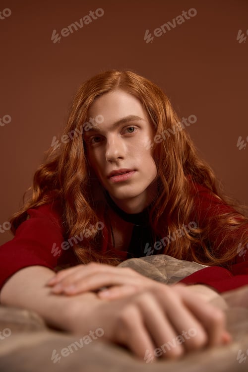 Preview: Elegant young man with long red hair showcasing stylish attire in an artistic setting