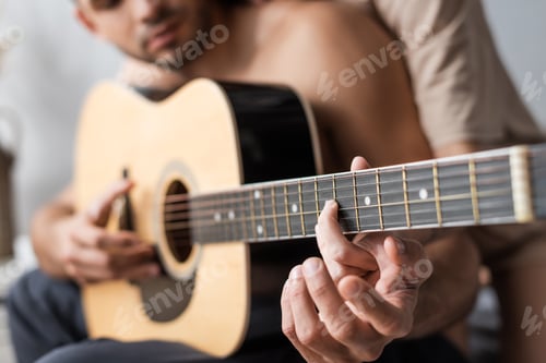 Preview: Cropped view of blurred couple playing acoustic guitar at home