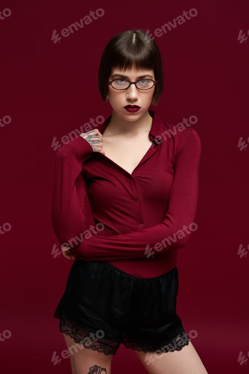 Preview: Fashionable young woman exuding confidence in stylish ensemble against bold red background