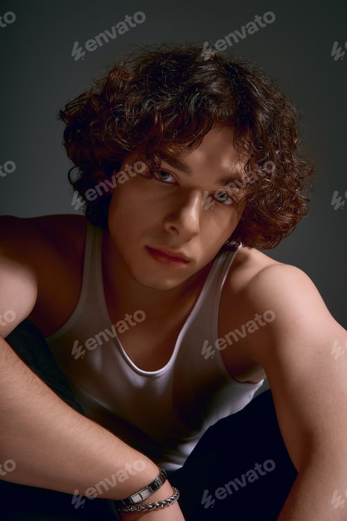 Preview: Young man with curly hair expresses deep emotion in fashionable attire and soft lighting