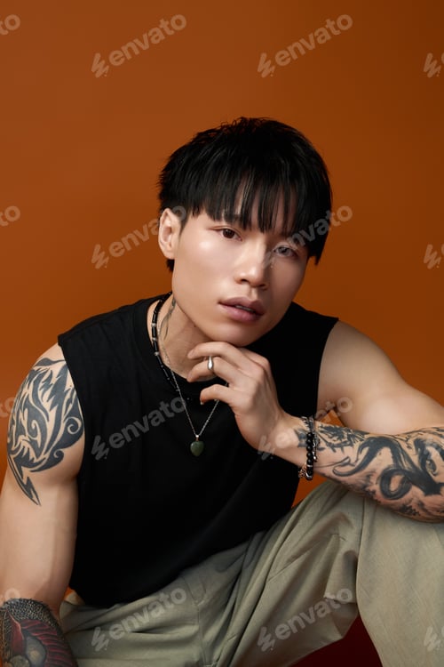 Preview: Young handsome man poses elegantly with tattoos against a warm orange backdrop capturing his allure