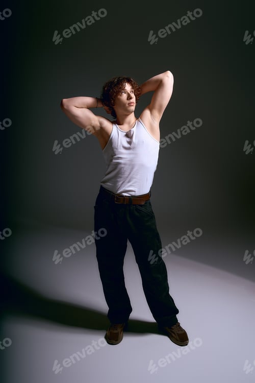 Preview: Emotional young man with curly hair expresses confidence in stylish outfit in artistic lighting