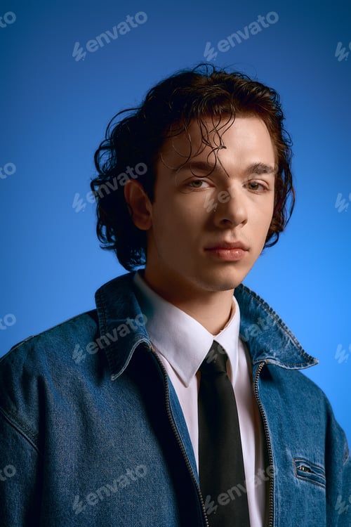 Preview: Young man with curly hair showcases stylish fashion against a vibrant blue background