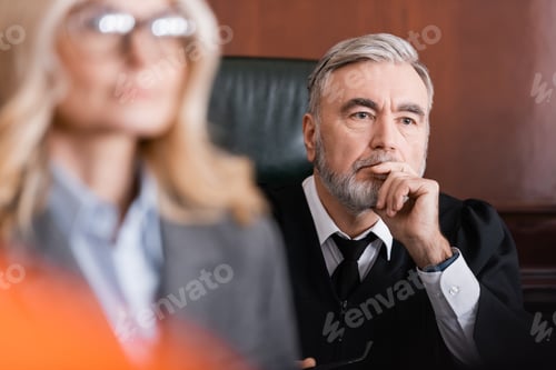 Preview: Senior Judge Holding Hand Near Face While Thinking Near Advocate on Blurred Foreground