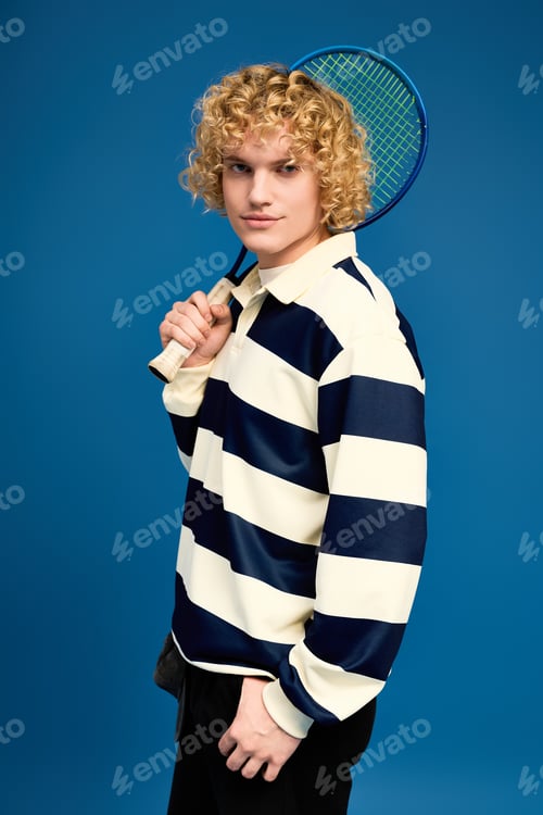 Preview: Young man with curly blonde hair showcases trendy style with a tennis racket