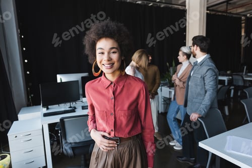 Preview: Happy African American Advertising Manager Looking at Camera Near Blurred Multicultural Colleagues