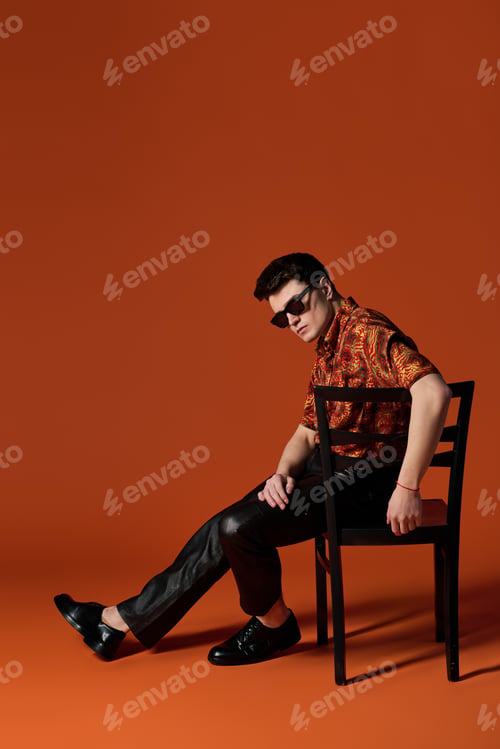 Preview: Handsome young man poses confidently against warm orange backdrop in stylish attire