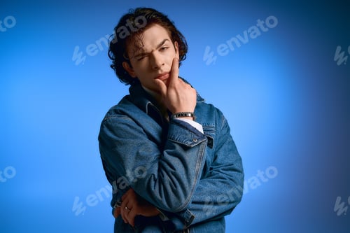 Preview: Expressive young man with curly hair showcases stylish fashion against a vibrant blue backdrop
