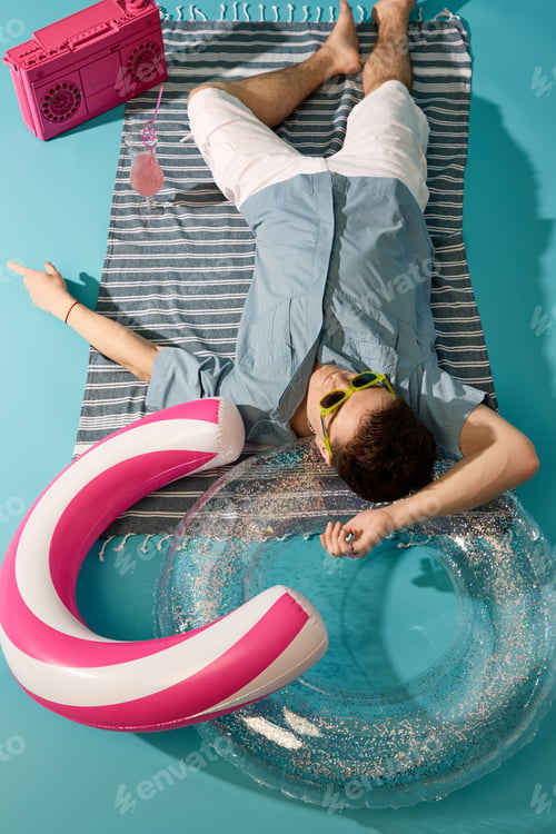 Preview: Stylish young man relaxing on summer day with colorful pool accessories and refreshing drink