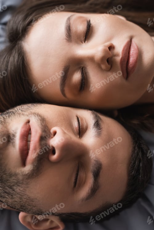 Preview: Top view of young couple with closed eyes lying on bed