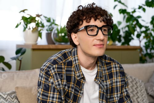 Preview: Curly young man enjoying a peaceful moment in his stylish apartment filled with plants