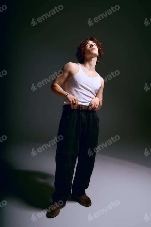 Preview: Young emotional man showcasing fashion in stylish attire against dark backdrop
