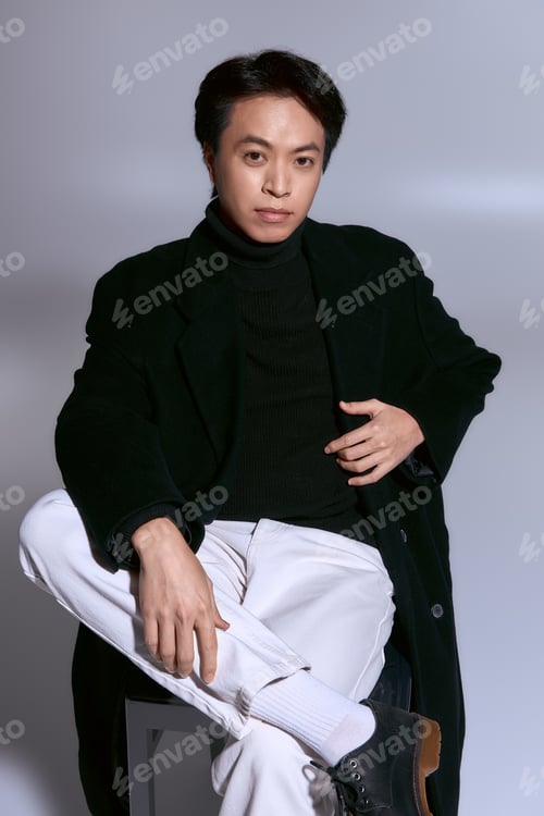 Preview: Stylish young man exudes confidence in a black coat and turtleneck in a modern studio