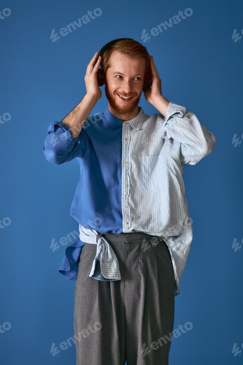 Preview: Handsome red haired man showcases stylish attire with headphones against a vivid blue backdrop