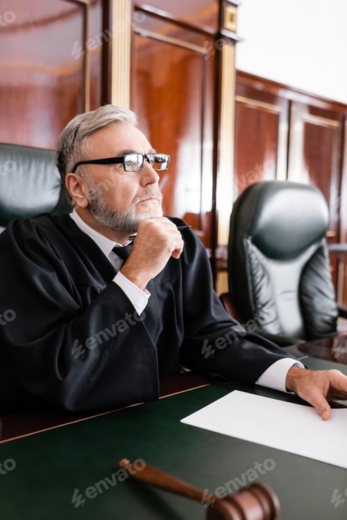 Preview: Senior Judge in Robe and Eyeglasses Sitting With Pen During Litigation