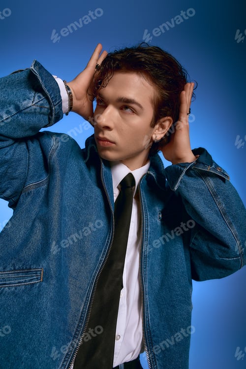 Preview: Emotional young man with curly hair showcases stylish attire against a vibrant blue backdrop