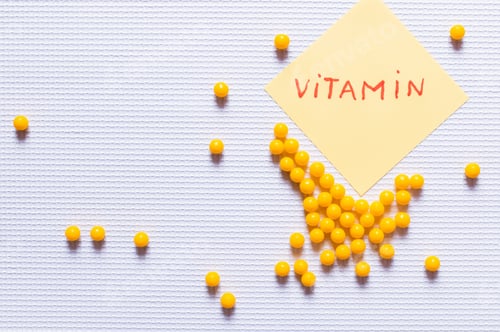Preview: Top View of Yellow Round Shape Medication Near Paper Note With Vitamin Lettering on White Textured