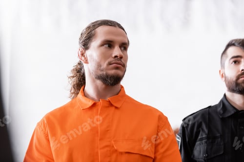 Preview: Accused Man in Orange Uniform Looking Away Near Bailiff in Court
