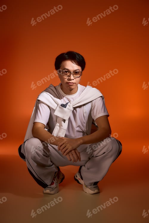 Preview: Stylish asian young man showcases his unique fashion sense in a vibrant studio setting