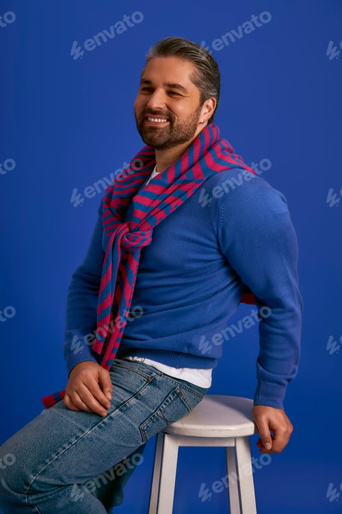 Preview: Stylish man in vibrant sweater enjoys casual moment on a blue background