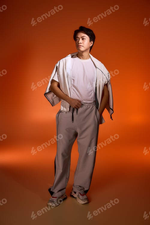 Preview: Stylish young man in studio showcases contemporary fashion in vibrant orange ambiance