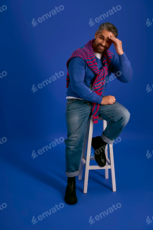 Preview: Stylish man poses against a vibrant blue backdrop, showcasing modern fashion trends