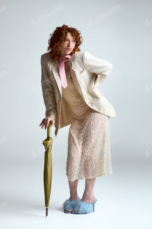 Preview: Stunning young woman showcasing eclectic fashion in a playful pose with an umbrella