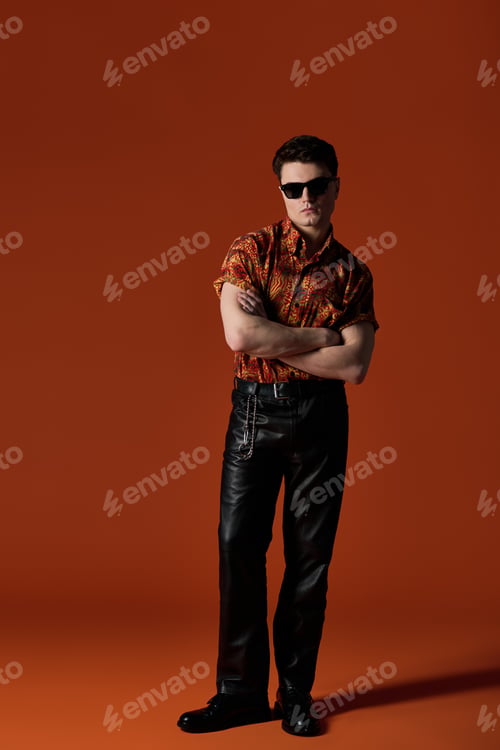 Preview: Stylish young man poses confidently against a vibrant orange backdrop showcasing modern fashion