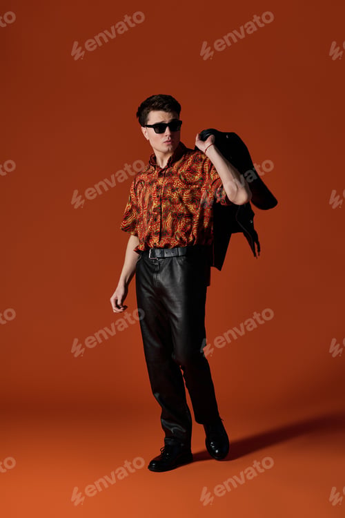 Preview: Handsome young man in vibrant fashion striking a confident pose against an orange backdrop