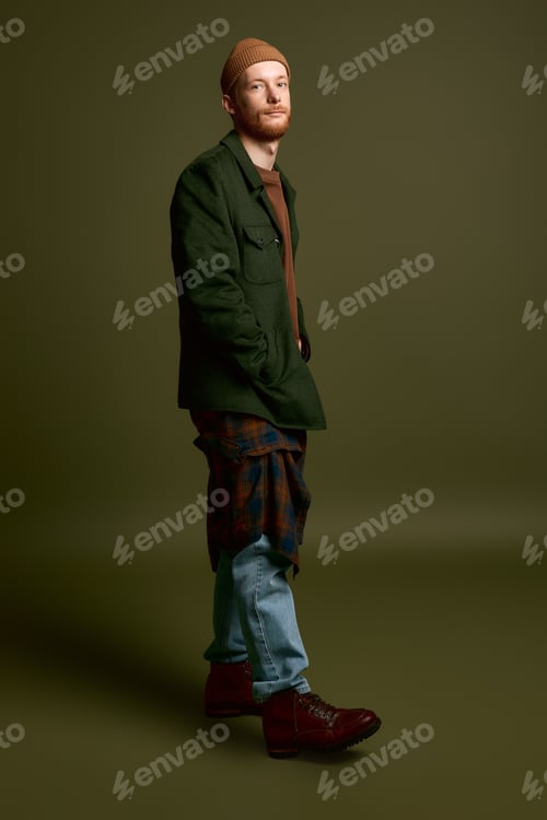 Preview: Stylish young man poses confidently against a muted green backdrop showcasing modern fashion