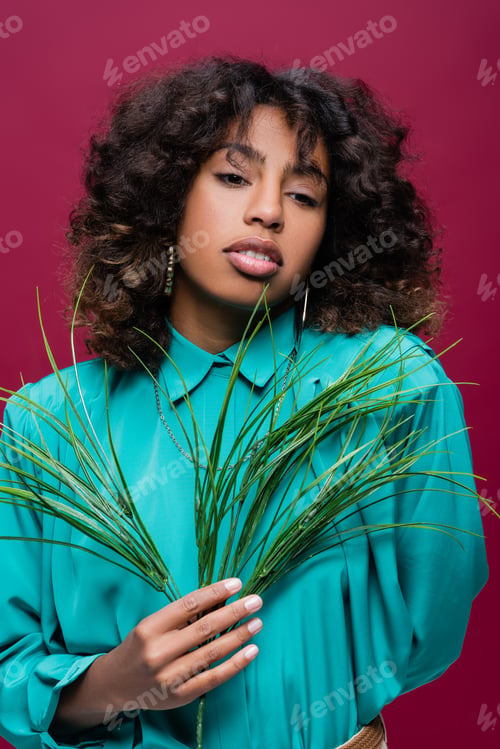 Preview: Curly African American Woman in Turquoise Blouse Holding Green Branch Isolated on Pink