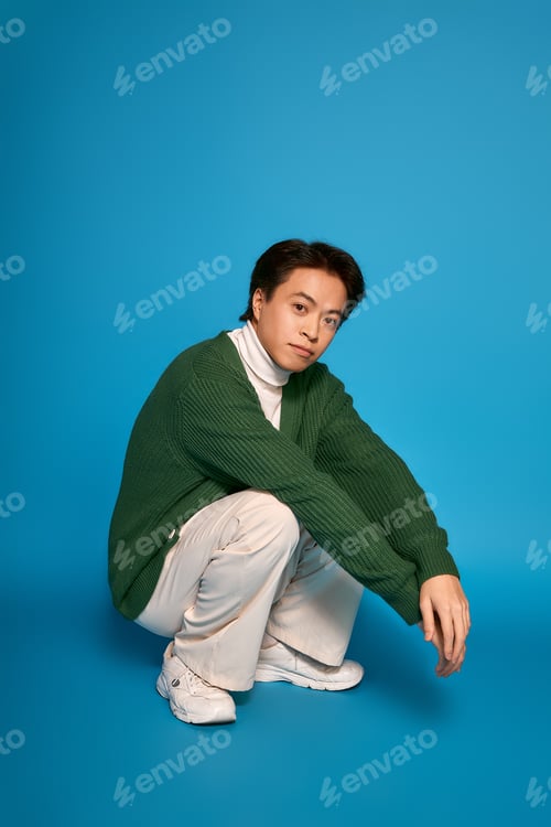 Preview: Stylish young man showcases his unique fashion sense in a vibrant studio setting