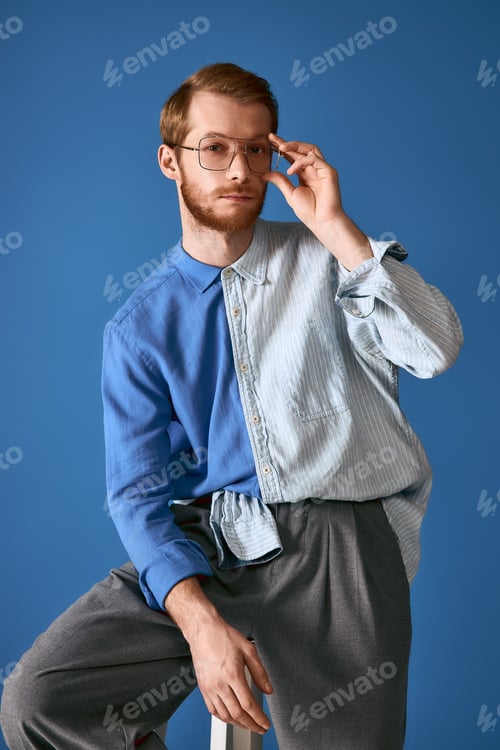 Preview: Handsome red haired man showcases stylish fashion with contemporary flair against a blue backdrop