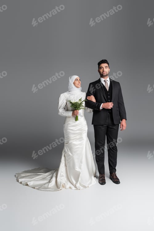 Preview: Full Length of Groom in Suit Standing With Happy Muslim Bride With Wedding Bouquet of Calla Lily